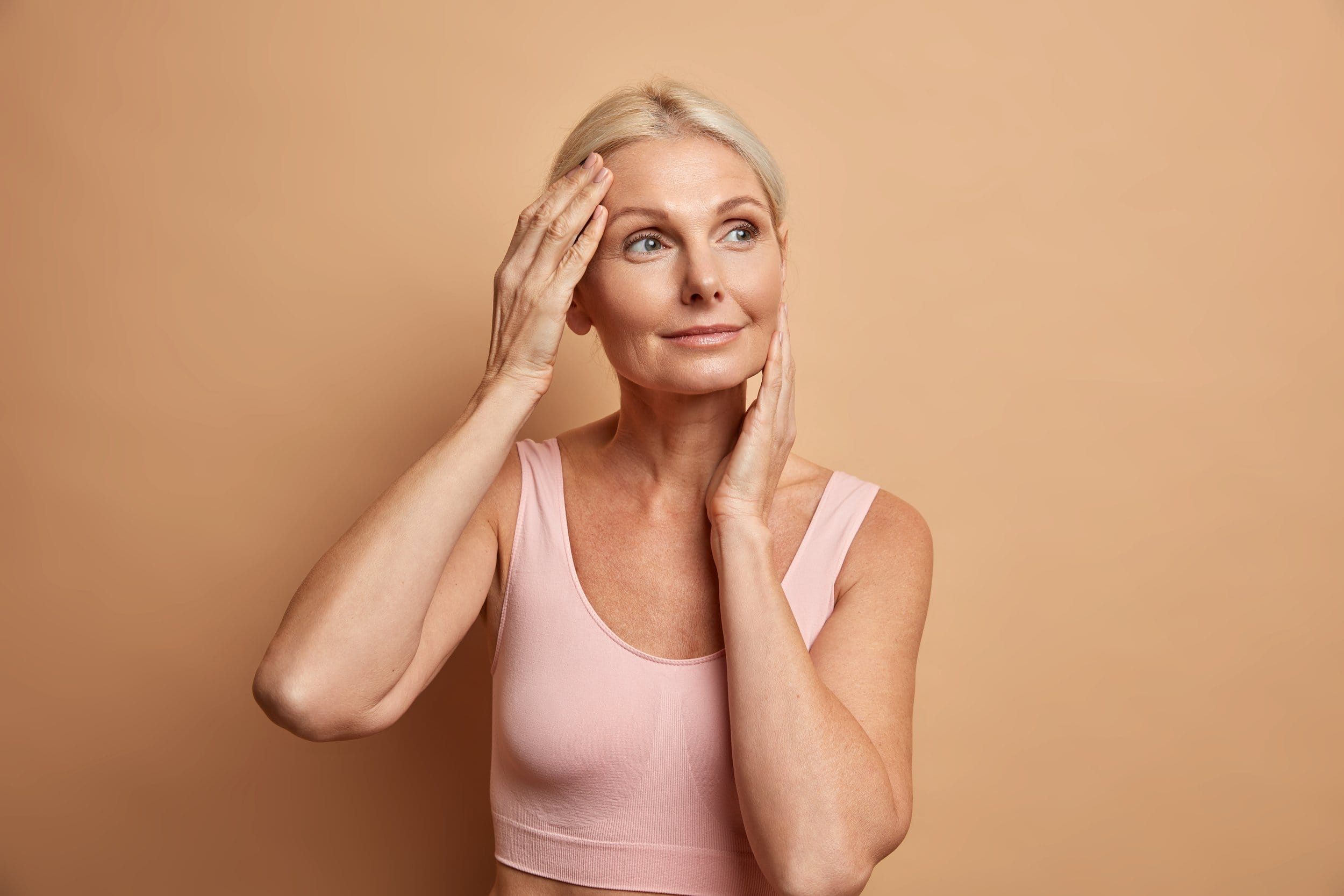 Portrait of mature elderly European woman touches face gently has perfect skin and looks thoughtfully away enjoys her soft complexion cares about appearance satisfied after anti aging procedure Woman after Botox treatment